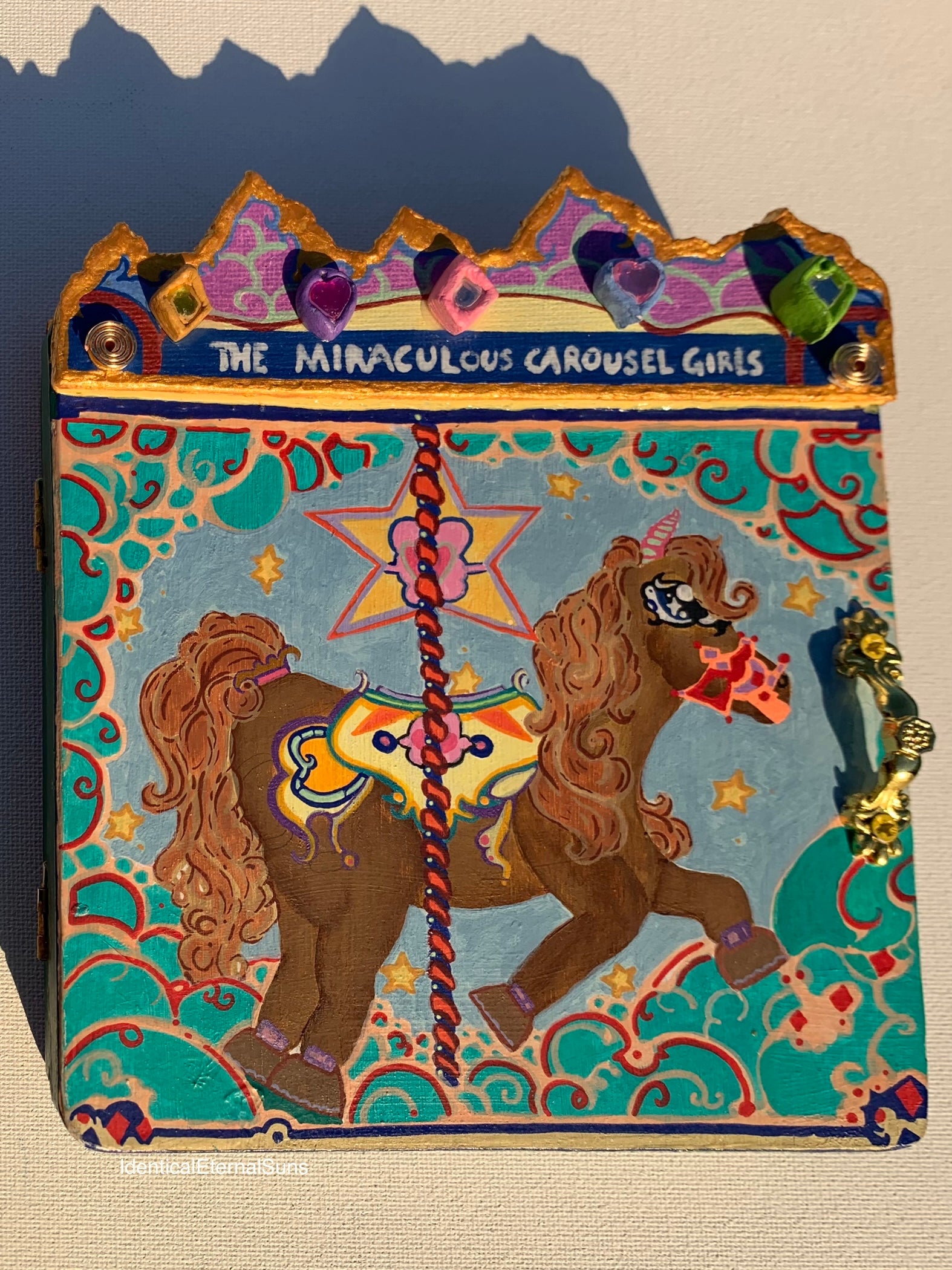 Decorative book cover with carousel design and text 'The Miraculous Carousel Girls'. Colorful carousel-themed pony mini painting artwork. The Miraculous Carousel Girls wooden painting book, vibrantart, equineart, carouselride, merrygoroundmagic, immersiveart, nostalgickidcore, hopefulart, innocentjoy, nurserydecor, babygirlroom, childlikemagic, playfulimagination, joyfulplaytime, majesticlookbook, nurserybabyart, babygirldecor, cherishablekeepsakes, functionalsurrealism, surrealismsculpture