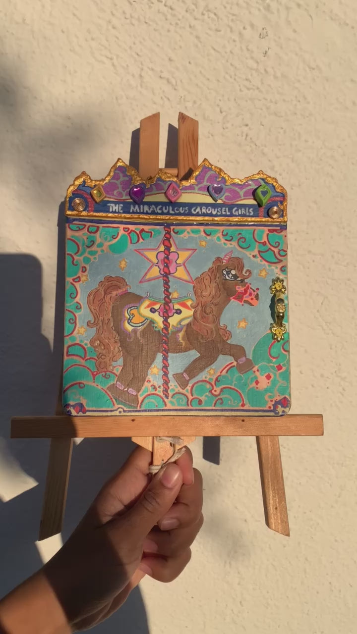 Colorful carousel-themed pony mini painting artwork. The Miraculous Carousel Girls wooden painting book, vibrantart, equineart, carouselride, merrygoroundmagic, immersiveart, nostalgickidcore, hopefulart, innocentjoy, nurserydecor, babygirlroom, childlikemagic, playfulimagination, joyfulplaytime, majesticlookbook, nurserybabyart, babygirldecor, cherishablekeepsakes, functionalsurrealism, surrealismsculpture
